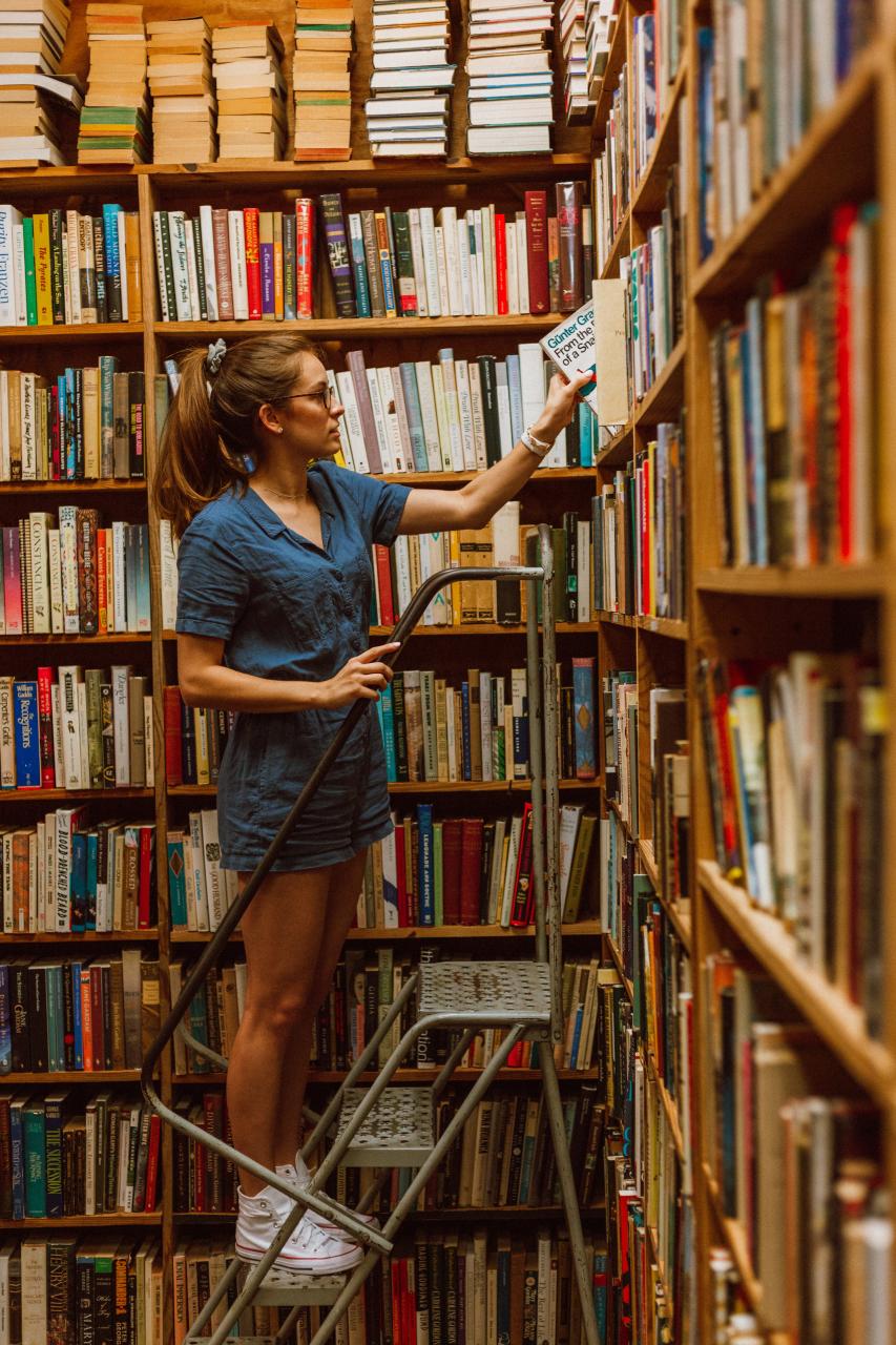 Junge Frau auf einer Leiter vor dem Bücherregal